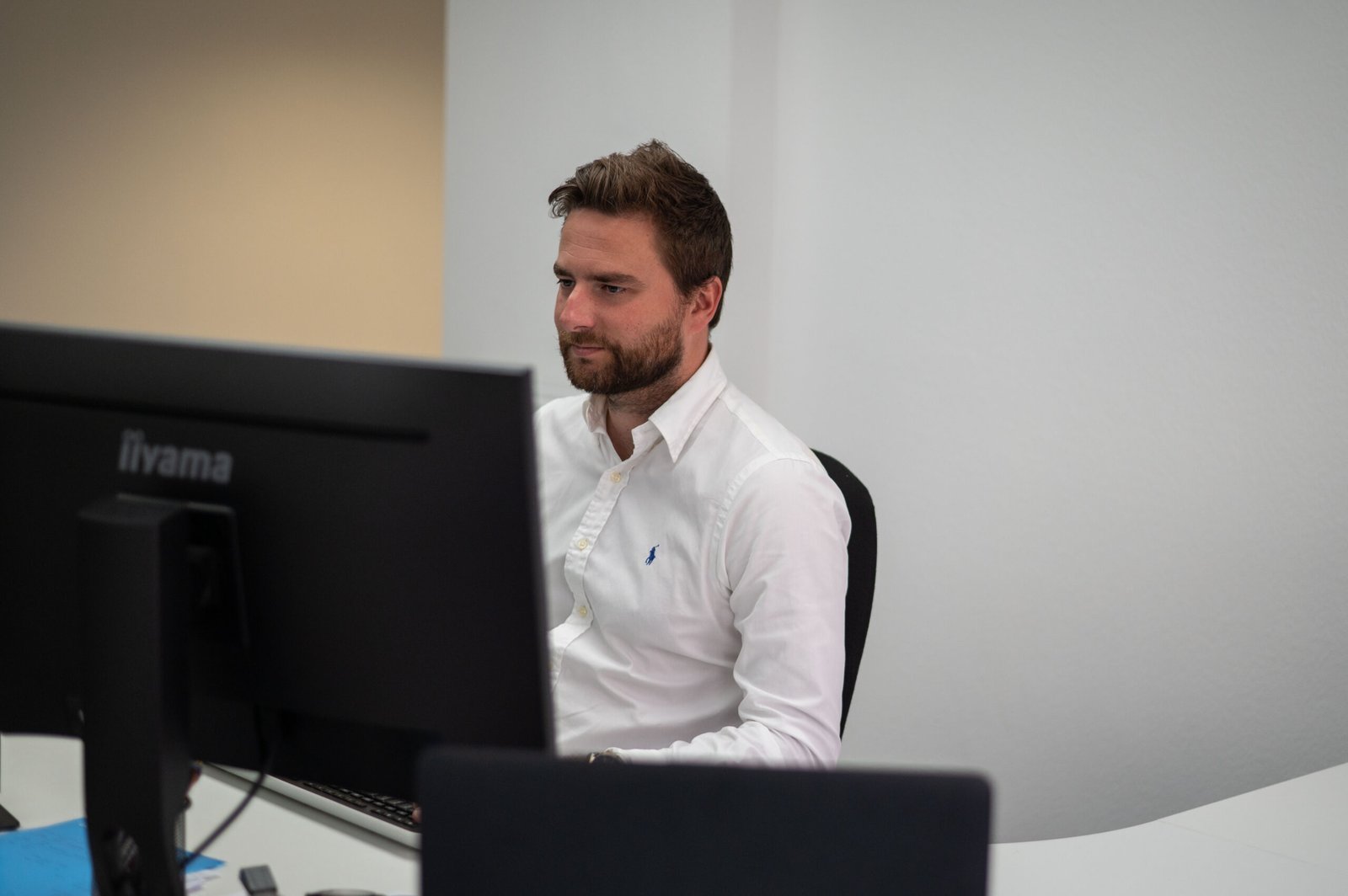 Een man in een wit shirt zit achter een bureau en werkt aan een computer in een modern kantoor.